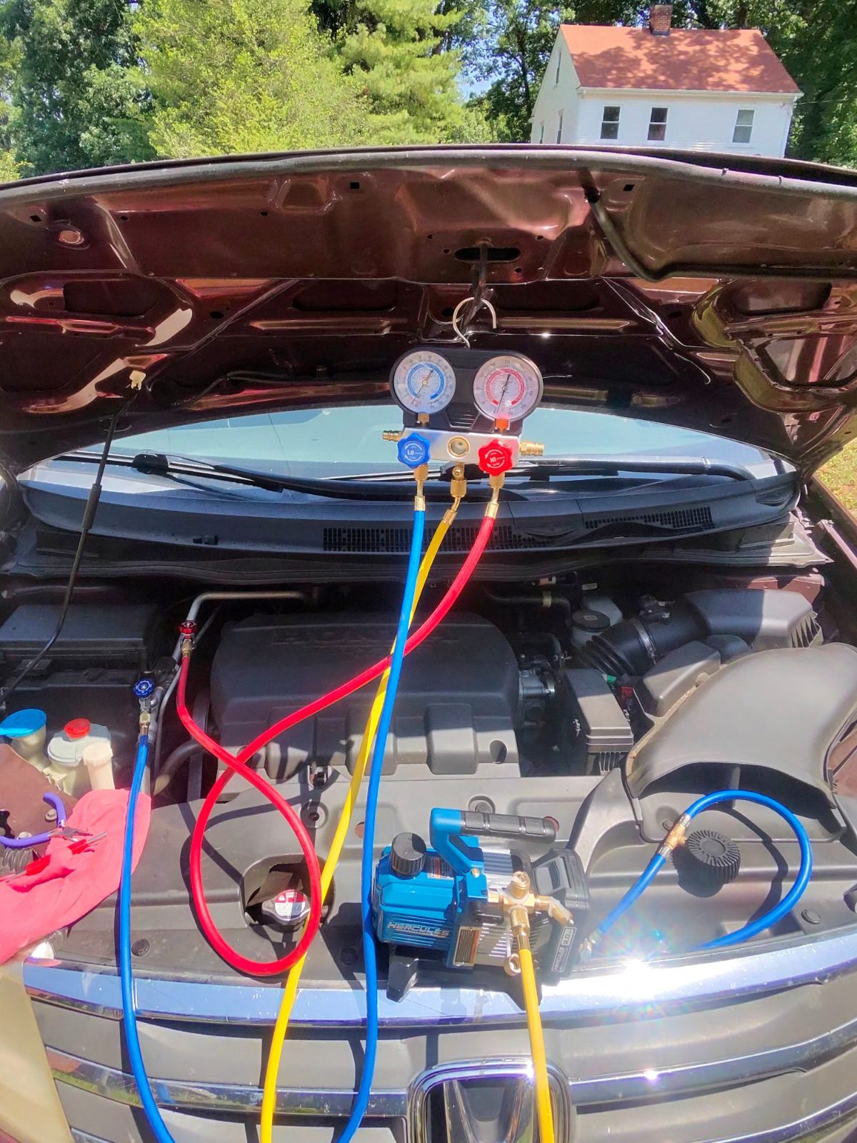 Air conditioning gauges and vacuum pump hooked up under the hood of a car outdoors