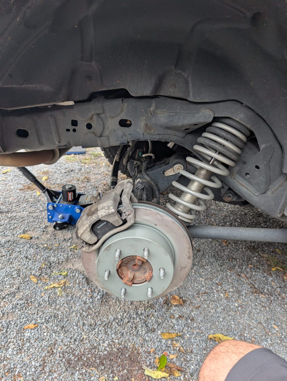 Wheel removed on a jacked up vehicle showing the brake rotor, caliper and coil spring