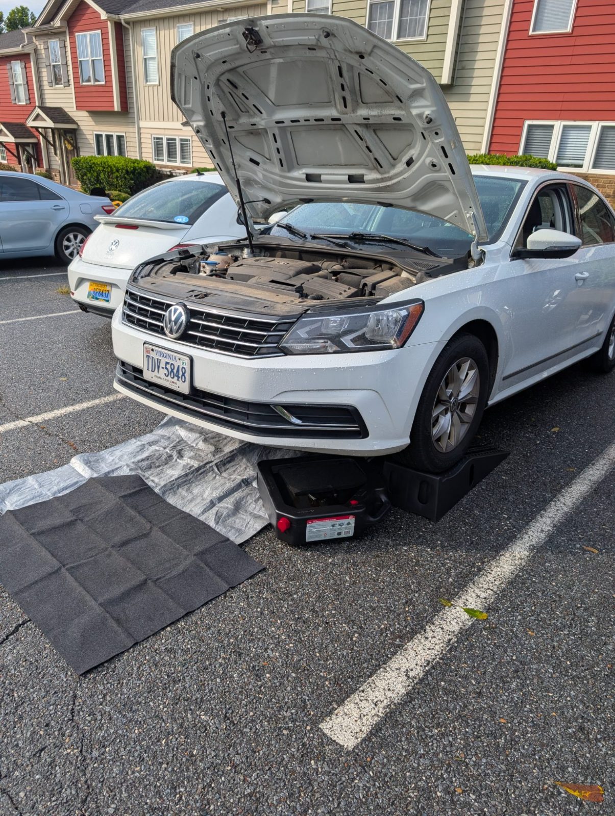 White sedan on ramps with hood raised and a drain pan under the front for an oil change