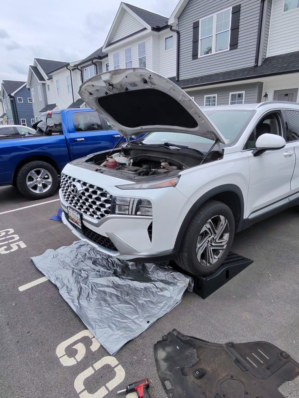White SUV on ramps in a parking space with hood open and underbody panel removed